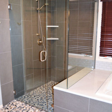 Completed shower with new shower trim tile surround quartz corner shelves pebble flooring glass shower doors