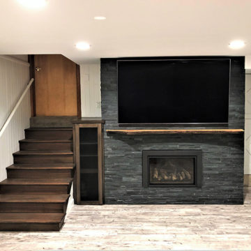 Completed basement remodel with-new fireplace surround custom mantel and cabinet stained stairs and updated ceiling and lighting