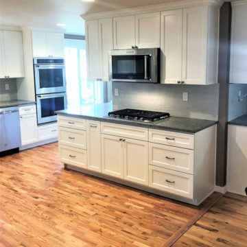 Completed kitchen remodel with an updated more open layout, custom cabinets, quartz countertops, tile backsplash, and new wood flooring